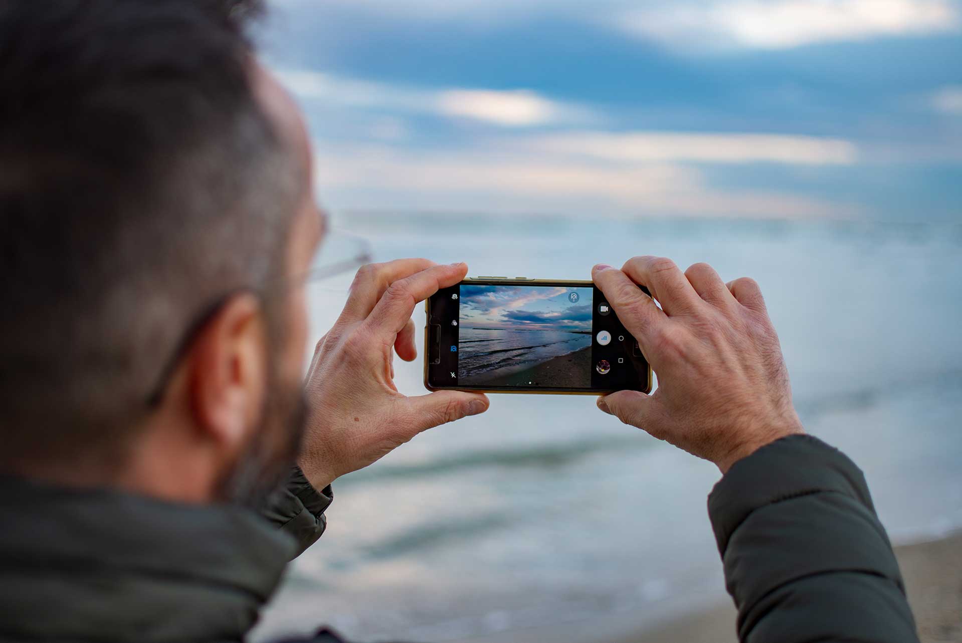 Homem fazendo fotos de uma praia com um celular em um fim de tarde.