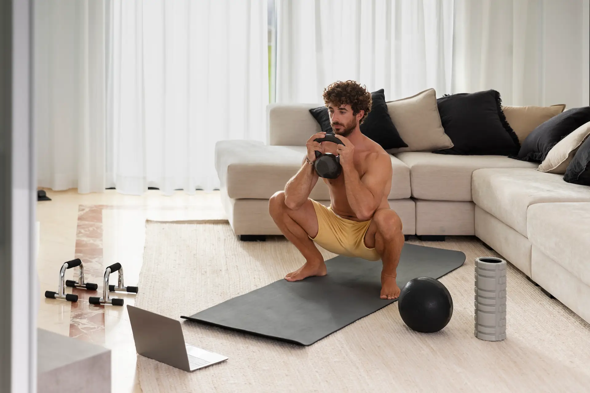 Homem segurando um kettlebell enquanto realiza um agachamento. Um ótimo exercício para treinar em casa