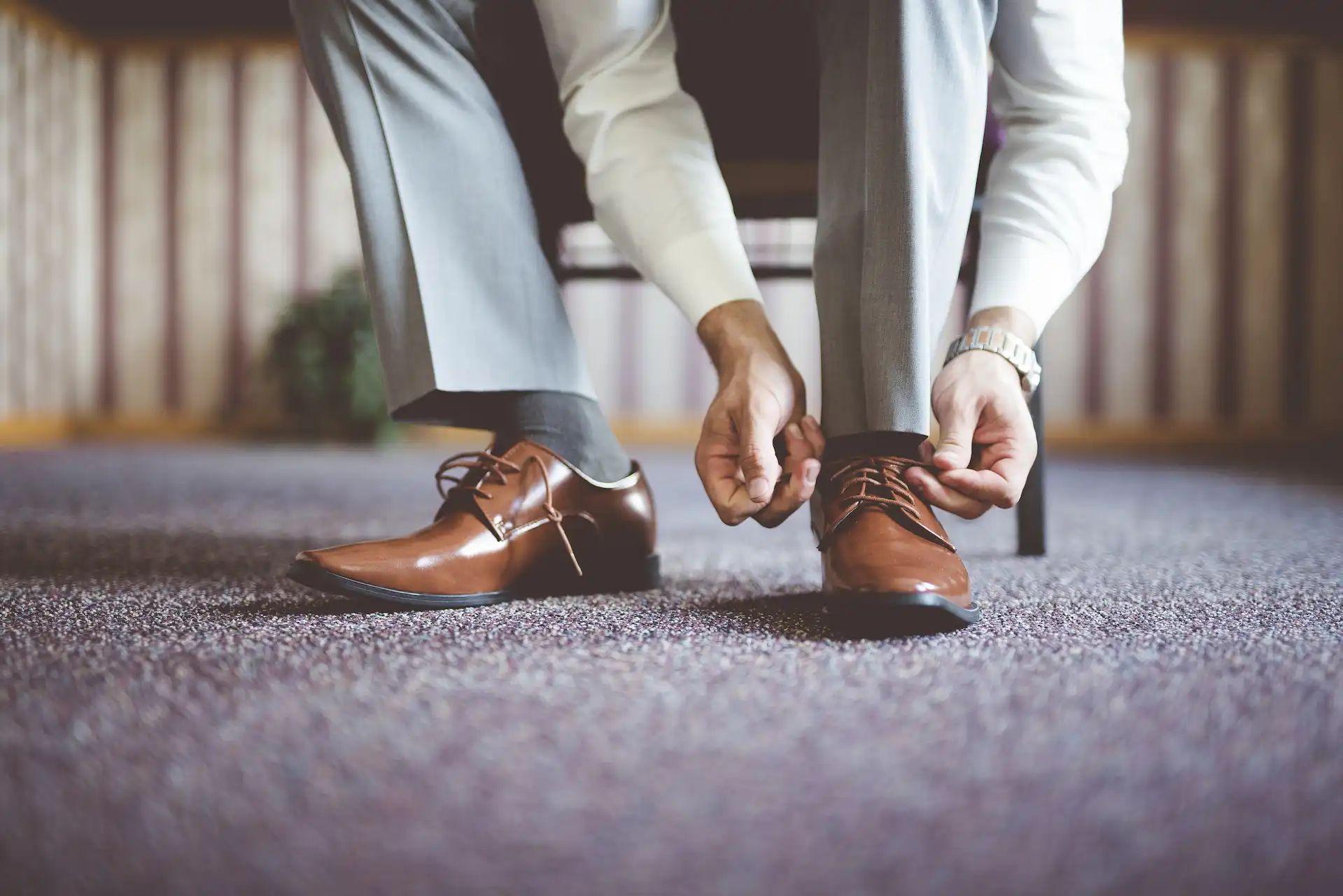 Mãos masculinas amarrando um sapato social de couro bege