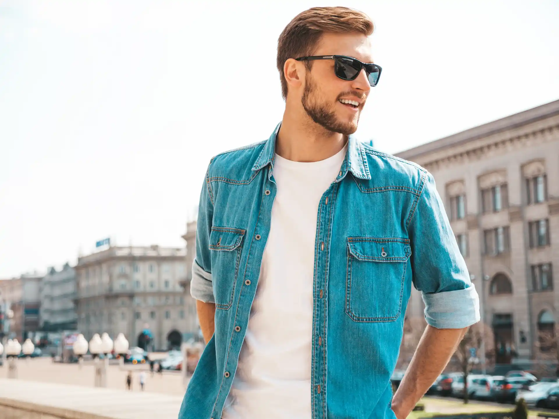 Homem utilizando camiseta branca lisa por baixo de uma jaqueta jeans azul, e óculos de sol. Um exemplo de look masculino casual