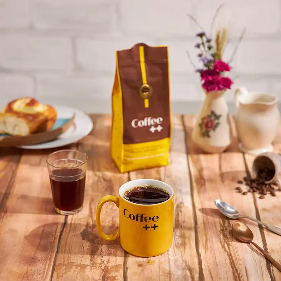 Embalagem do Coffee Mais Super Especial sobre uma mesa, ao lado de uma caneca e um copo americano cheios de café.