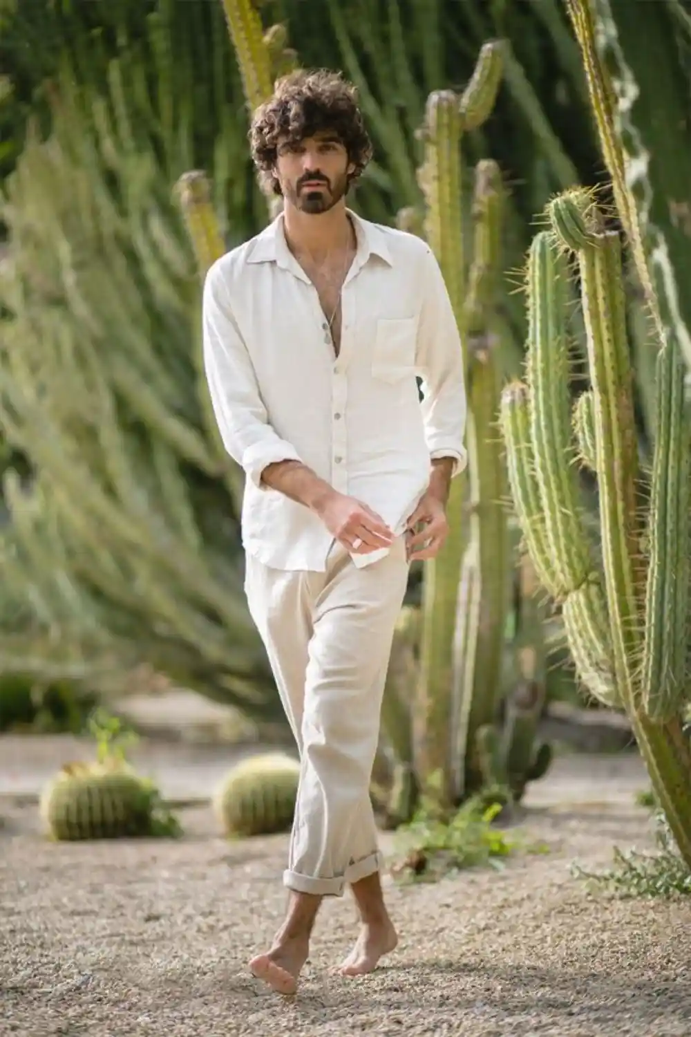 Homem utilizando camisa leve, com botões abertos no peito e calça leve. As peças são na cor bege clara.