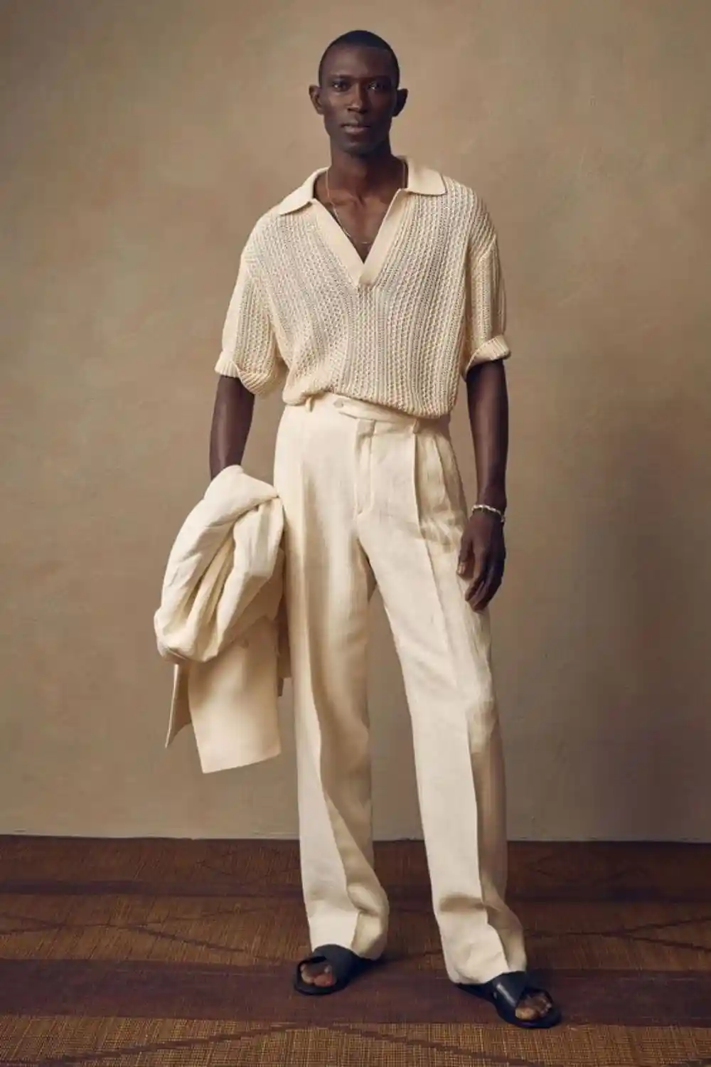 Homem utilizando uma camiseta de tecido que lembra crochê, calça e chinelo.