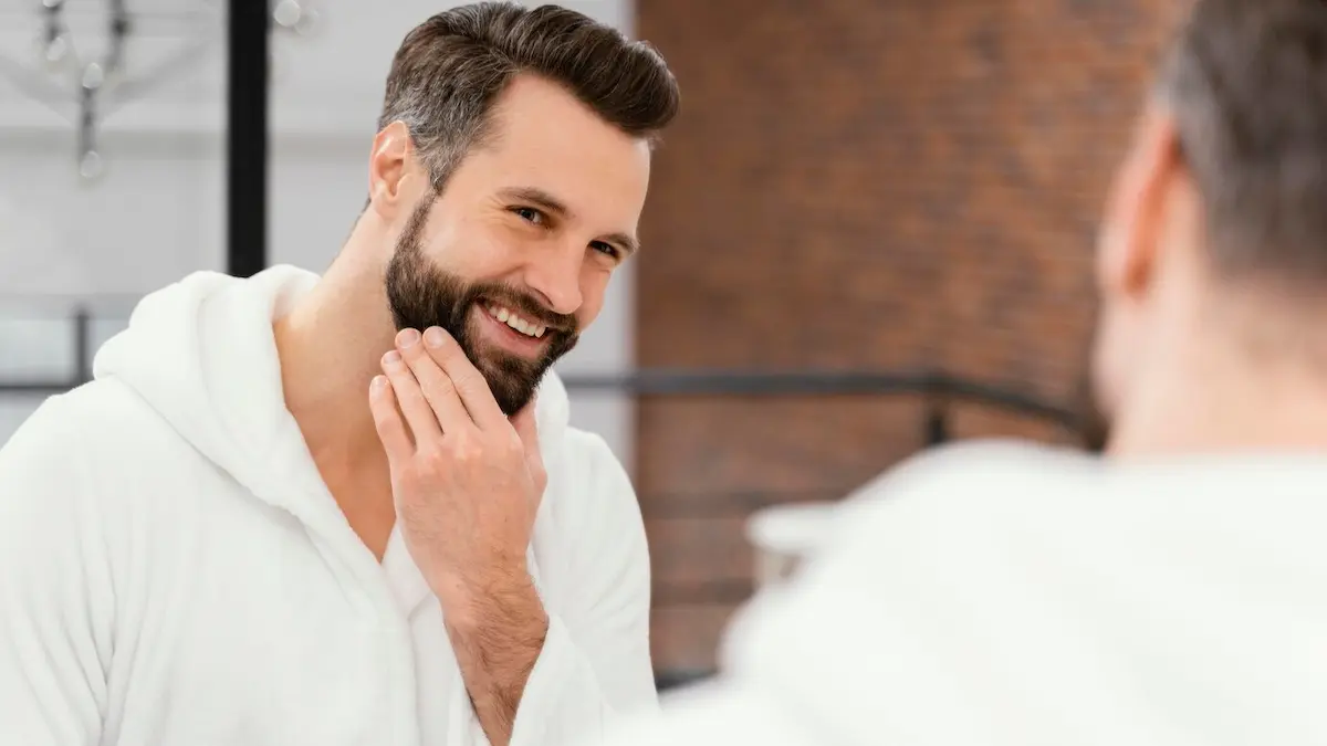 Homem barbudo se olhando no espelho após cuidar da barba.