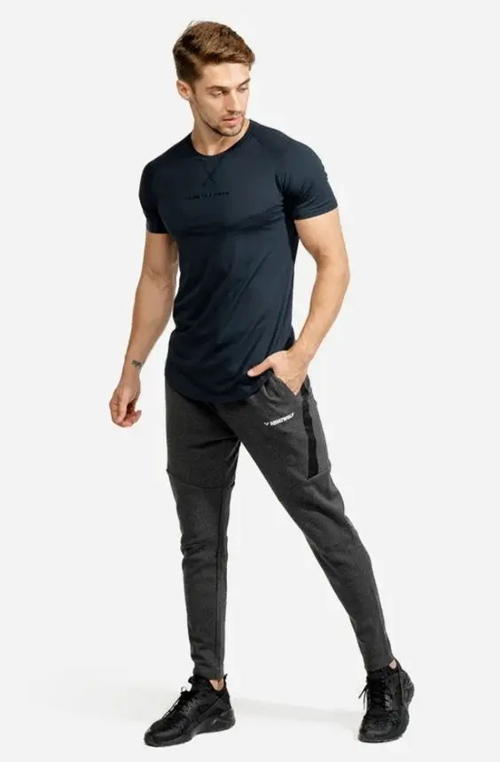 Homem utilizando um look monocromático cinza-escuro no estilo esportivo urbano. Ele usa calça jogger, camiseta e tênis.