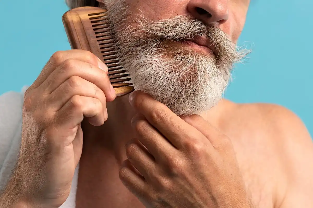 Homem penteando a barba. Esse é um passo fundamental de como aparar a barba.