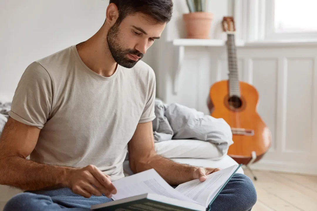 Homem sentado no chão lendo um livro.