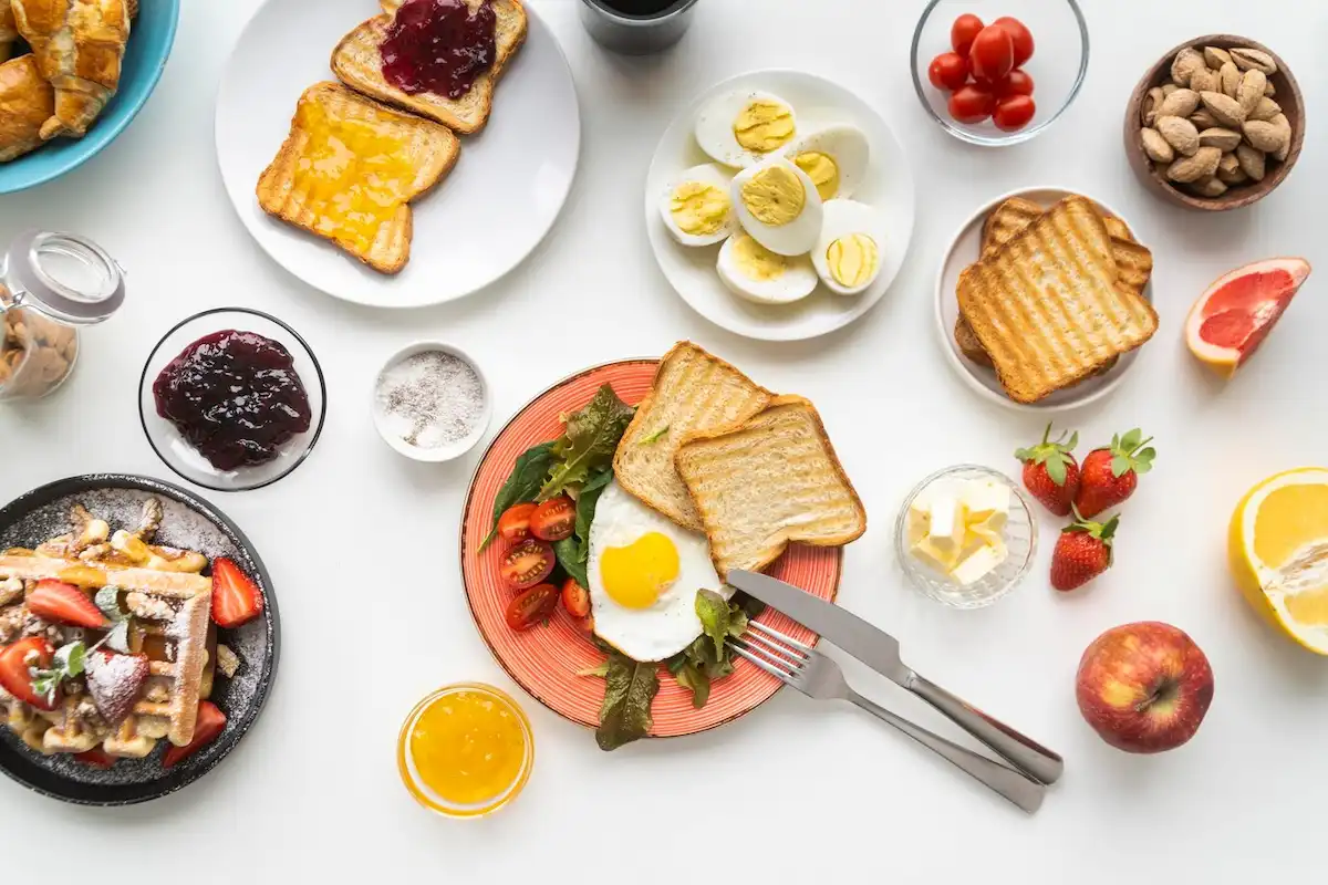 Diversos alimentos de um café da manhã. Torradas, ovos, geleias, frutas, entre outros.