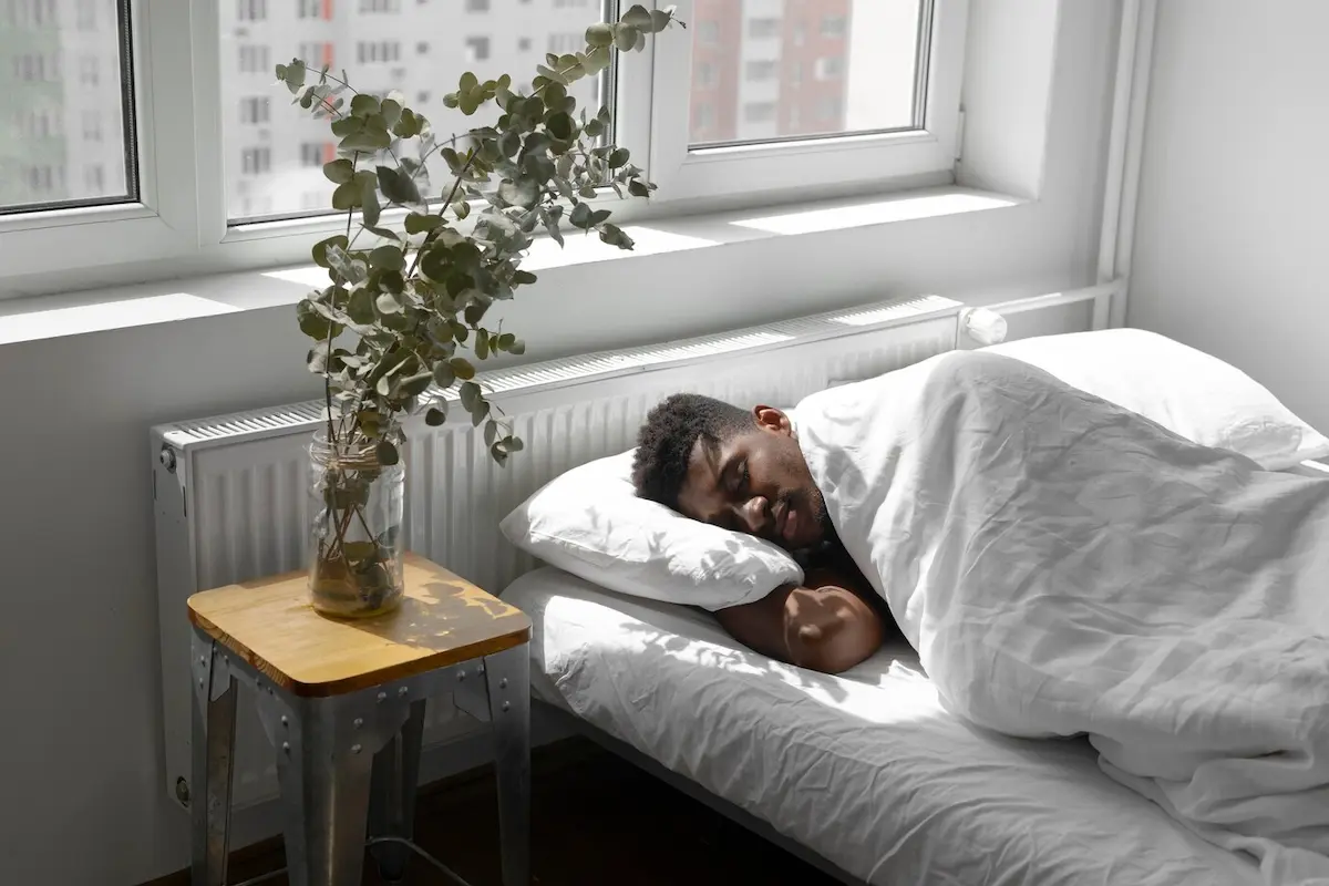 Homem dormindo em uma cama com lençóis e travesseiros brancos.